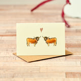 Greeting card with two Highland cows and a heart on a wooden surface
